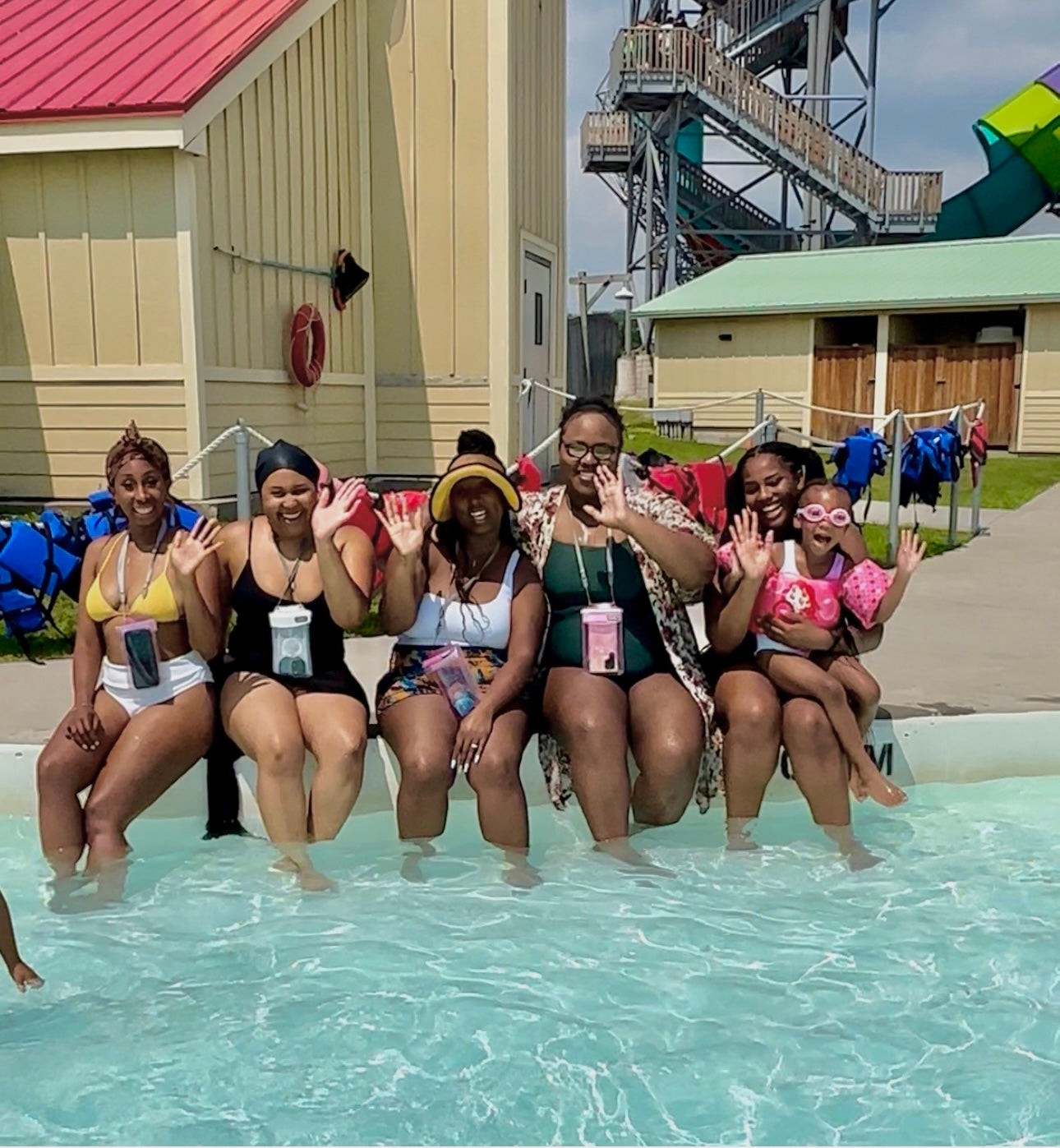 A group of women and a child sitting together at the edge of a swimming pool.