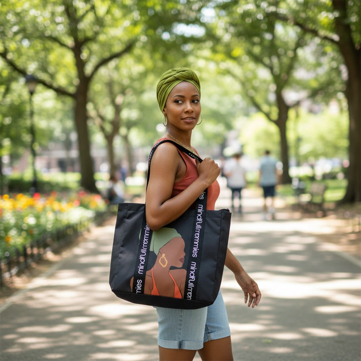 Woman in a park holding a black Mindfull Mommies tote bag with a design